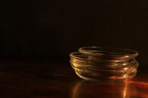 暗い机にずれて重なった透明なガラスの器。タグが重ねて付くため絞り込みが効かないことの比喩