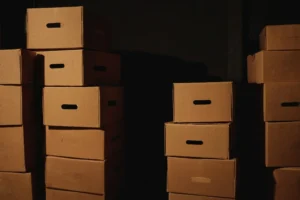 暗い部屋に積み上がった未開封の箱。増え続けるのに手をつけられないことを表した比喩